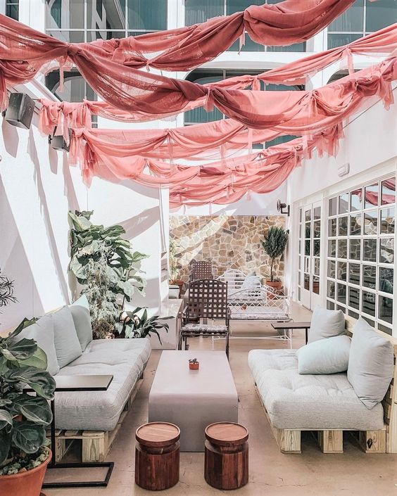 a beautiful neutral terrace with neutral pallet furniture, a low coffee table and side tables, metal and forged furniture, pink garlands over it