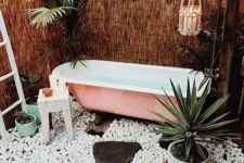 a boho chic outdoor space with tall woven walls, candles, pebbles, a pink bathtub and potted plants for a fresh feel