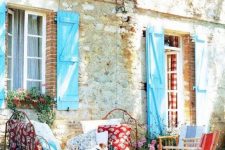 a bright and colorful Provence terrace with a forged bed with colorful cushions and pillows, a stained table and some neutral chairs with colorful pillows and cushions