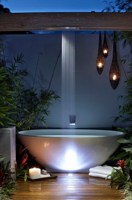 a chic contemporary space with an oval tub, a waterfall shower, some drop-shaped candle lanterns and greenery around
