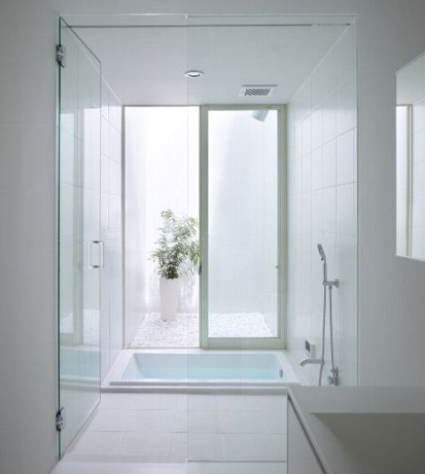a clean white bathroom with a sunken bathtub, a skylight, potted greenery and a sink is very minimal and simple