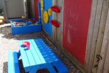 a colorful play area with a bright blue sand box, some plastic decor on the fence and a bright blue dining set