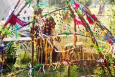 a colorful teepee covered with yarn, pompoms, buntings, flags and other bright stuff plus potted greenery
