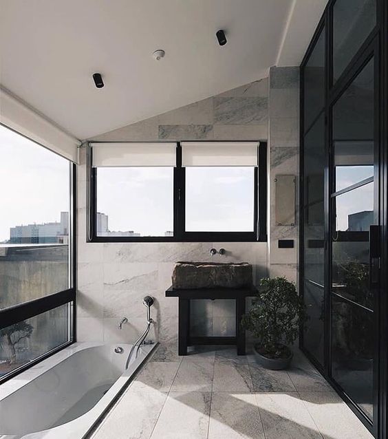 a contemporary bathroom in black and neutrals, with a rough stone sink, a sunken bathtub with a gorgeous panoramic view