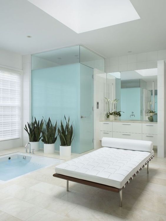 a contemporary bathroom in white and light blue, with a sunken bathtub and a leather couch plus potted plants for an outdoorsy feel