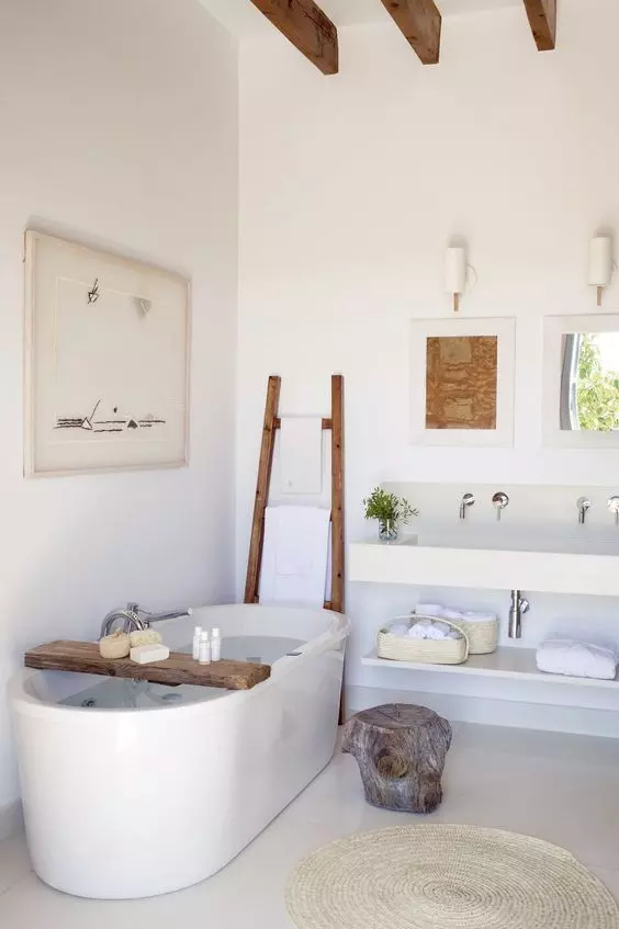 A contemporary coastal spa bathroom with an oval tub with a wooden shelf, a ladder for towels, a floating vanity and a wall mounted sink, a white jute rug