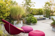 a contemporary terrace with lots of greenery, built-in benches, a fuchsia wicker chair, fuchsia poufs and a green cushion