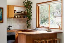 a cozy modern kitchen with light-stained cabinets, butcherblock countertops, an aqua tile backsplash and a large window with a garden view