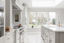 a dove grey kitchen with shaker style cabinets, white stone countertops, a large skylight and windows that open on the garden