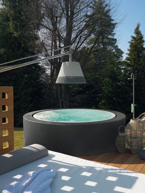 a hot tub clad with a matte black surface, with some candle lanterns and a daybed by its side