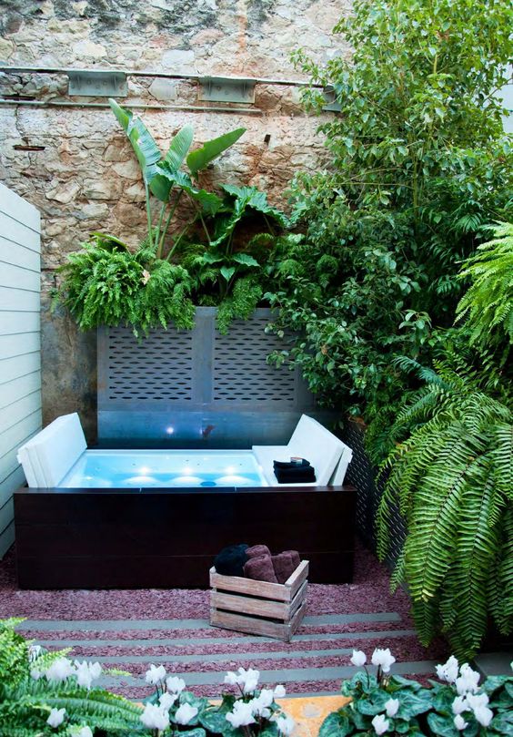 a jacuzzi, lush greenery around it, a crate with towels and some blooms for a welcoming space
