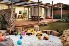 a large sand box with tree stumps and stones around looks very natural and bright with fun toys