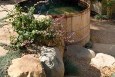 a large wooden tank is used as a plunge pool and looks very natural in rocks, greenery and blooms growing around