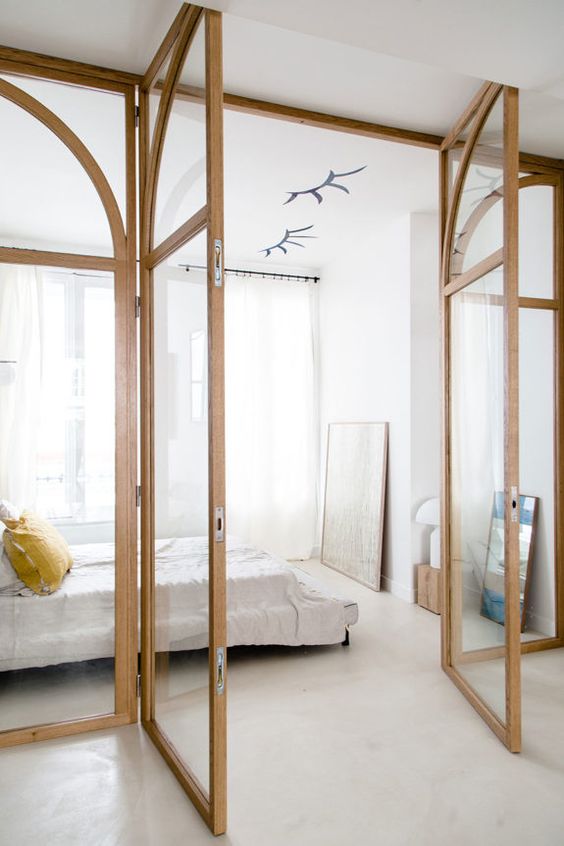A light filled neutral bedroom with glass walls, a bed, a mirror and some art is very cool and feels very airy