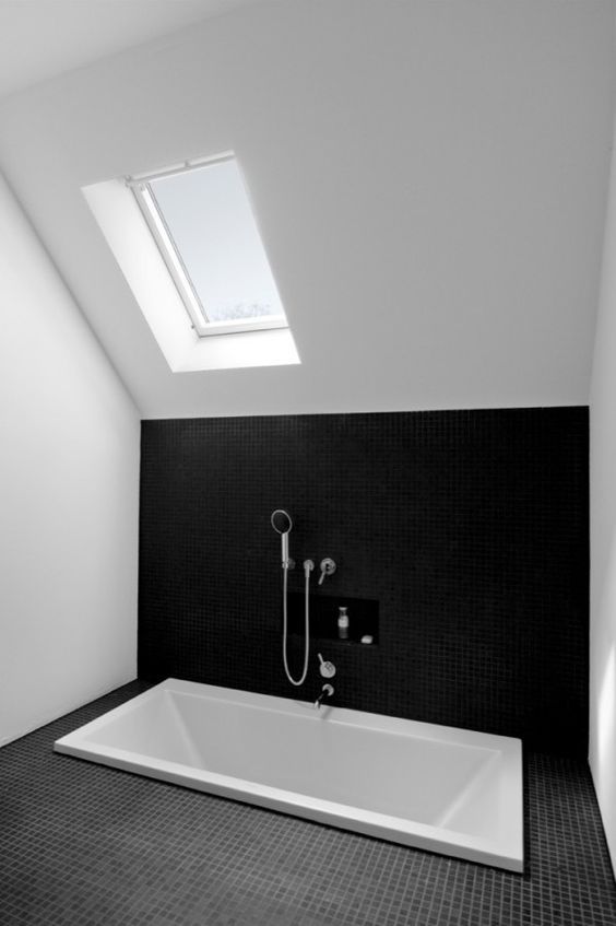 a minimal monochromatic bathroom in black and white, with skylights and a sunken bathtub is a very simple and stylish space