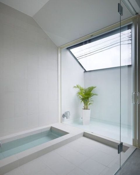 a minimalist bathroom with a skylight, a sunken bathtub, a shower space and a potted plant is clad with neutral tiles