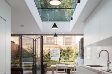 a minimalist white kitchen with a lovely dining zone and a skylight plus a glazed folding wall that allows to unite the space with a small private garden