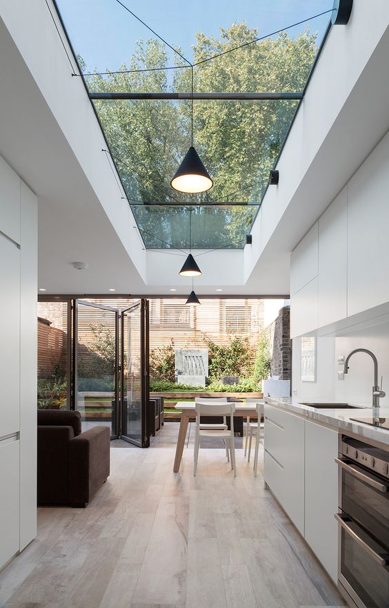 a minimalist white kitchen with a lovely dining zone and a skylight plus a glazed folding wall that allows to unite the space with a small private garden