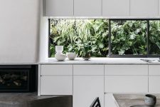 a minimalist white kitchen with sleek cabinets, white stone countertops, a window backsplash that opens on the tropical garden