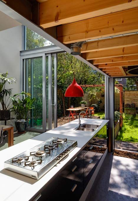 a modern black kitchen with glossy cabinets, a red pendant lamp and a glass wall with sliding doors to connect to the garden