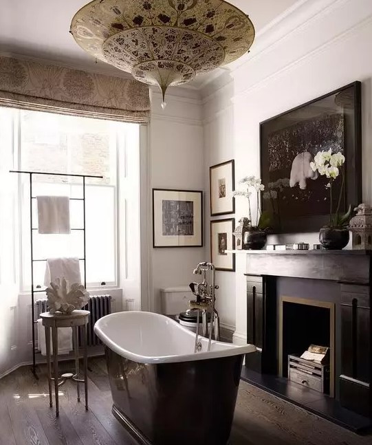 a moody vintage bathroom with a dark floor, a black fireplace, a black bathtub, a Moroccan pendant lamp and a gallery wall