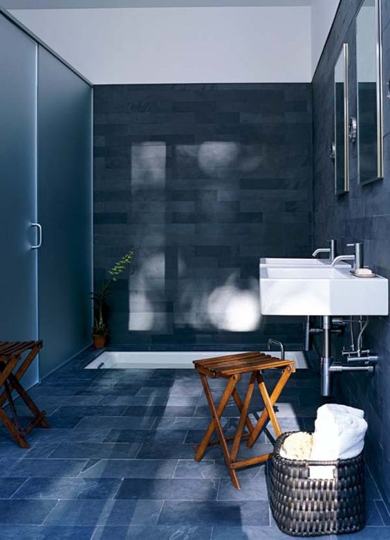 a navy and grey bathroom with a white sunken tub and sinks plus wooden folded stools and a basket for storage