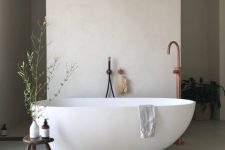 a neutral contemporary home spa with light grey concrete walls and a floor, an irregular shape tub, a jute rug and a copper faucet