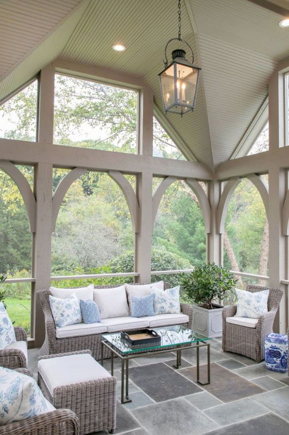 a neutral screened patio with wicker furniture with blue and white pillows, a glass coffee table and potted greenery