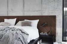 a rough cement accent wall is softened with a brown upholstered headboard and a fluffy rug on the floor