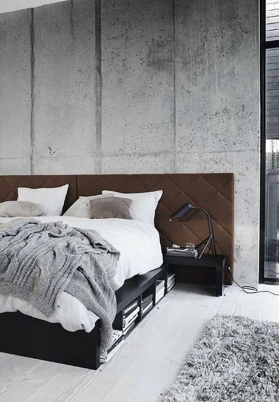 a rough cement accent wall is softened with a brown upholstered headboard and a fluffy rug on the floor