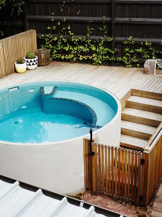 a round plunge pool with a wooden deck and some greenery in pots and on the wall make up a cool small spa