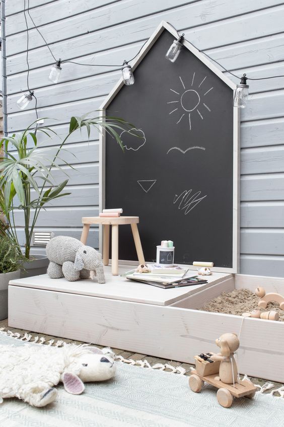 a simple Nordic outdoor play space with a chalkboard, a reading nook, a small sand box and a deck with toys