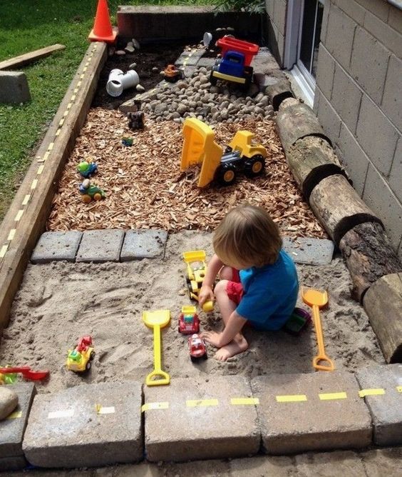 a simple outdoor oasis with a sand box, pebbles and a toy space is built of usual materials that most of have at hand