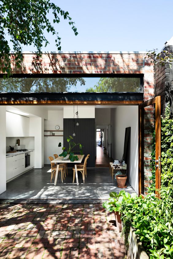 a small Scandi kitchen in white, with a stained furniture dining zone and a black accent wall plus a garage door to connect to the garden