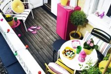 a small colorful terrace with simple bright furniture, colorful and striped textiles, storage units and potted greenery and blooms