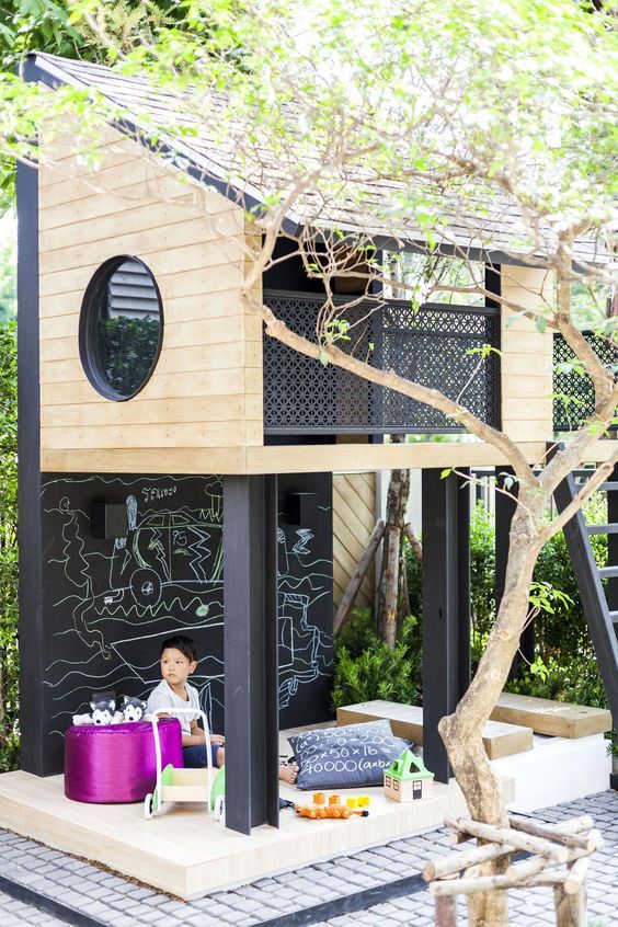 a stylish modern tree house with a ladder and a small yet cozy play space under it, with toys, pillows and other stuff