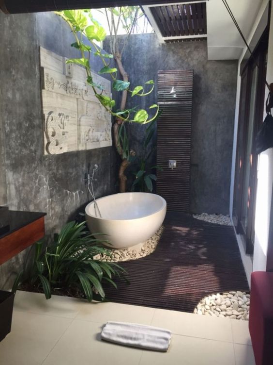 a tiny outdoor space with a wooden deck, pebbles, a shower, a bathtub and greenery growing plus a skylight