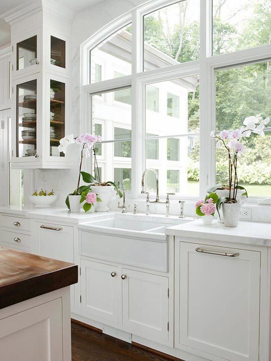 an elegant white kitchen with shaker style cabinets, white stone countertops and an arched window with garden views