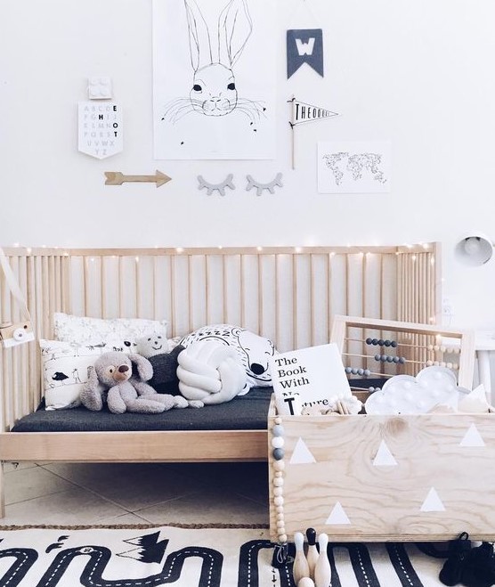 a Nordic kid's room with a wooden bed and a wooden box for toys, a printed rug, a gallery wall with artworks and not only