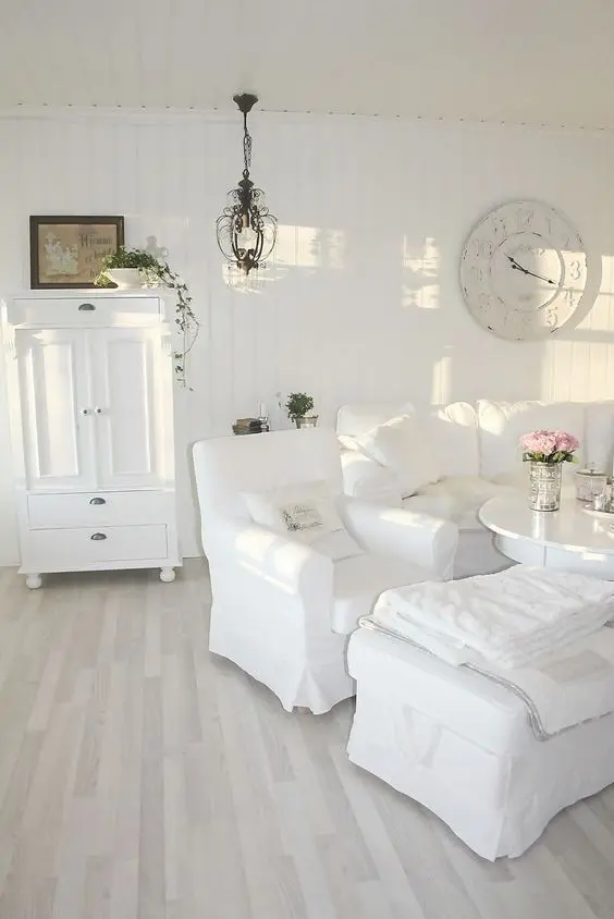 a beautiful white shabby chic living room with stylish vintage furniture, a clock, a chandelier and greenery in pots