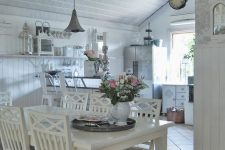 a beautiful white shabby chic space with white cabinets, a white dining set, a crystal chandelier and vintage decor on open shelves