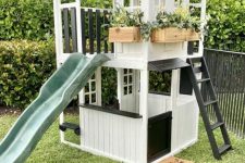a black and white kids’ playhouse with a ladder and a green slide, with potted greenery and blooms will be loved by your kids