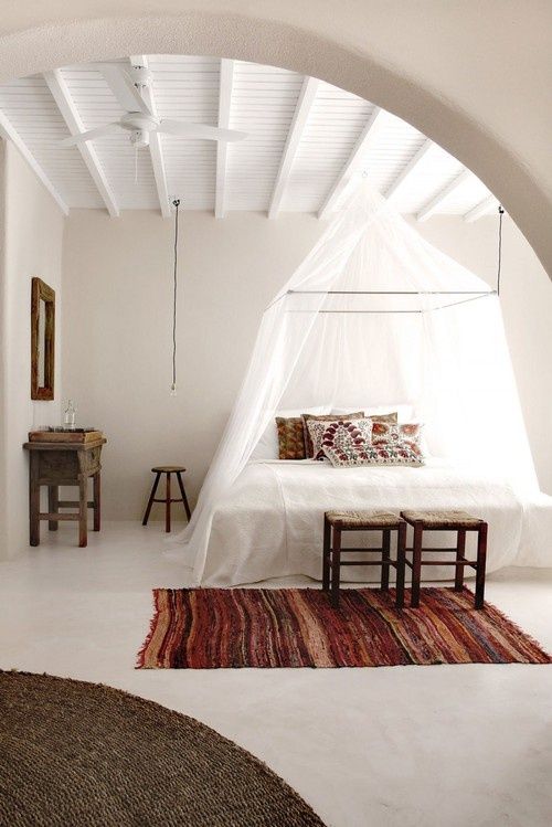 a boho chic bedroom with boho rugs, folksy pillows and a mosquito net canopy over the bed