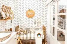 a boho neutral nursery with a gilded crib, a white dresser that is a changing table, some baby furniture and a wall-mounted shelf