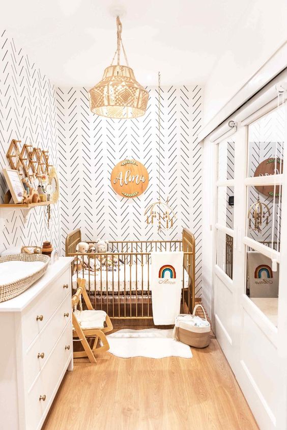 A boho neutral nursery with a gilded crib, a white dresser that is a changing table, some baby furniture and a wall mounted shelf