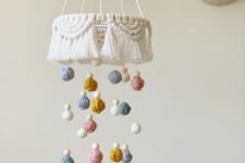 a boho yarn baby mobile with a macrame piece, colorful yarn balls and beads is a stylish idea for a boho space