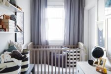 a chic tiny nursery with a stained crib, a white dresser and a black one, a striped rug and printed bedding, a wall-mounted shelf and toys
