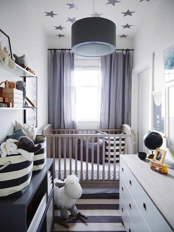 A chic tiny nursery with a stained crib, a white dresser and a black one, a striped rug and printed bedding, a wall mounted shelf and toys