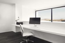 a clean minimalist home office in white, with a dark floor, a window with a view, a floating windowsill desk and a cool white chair