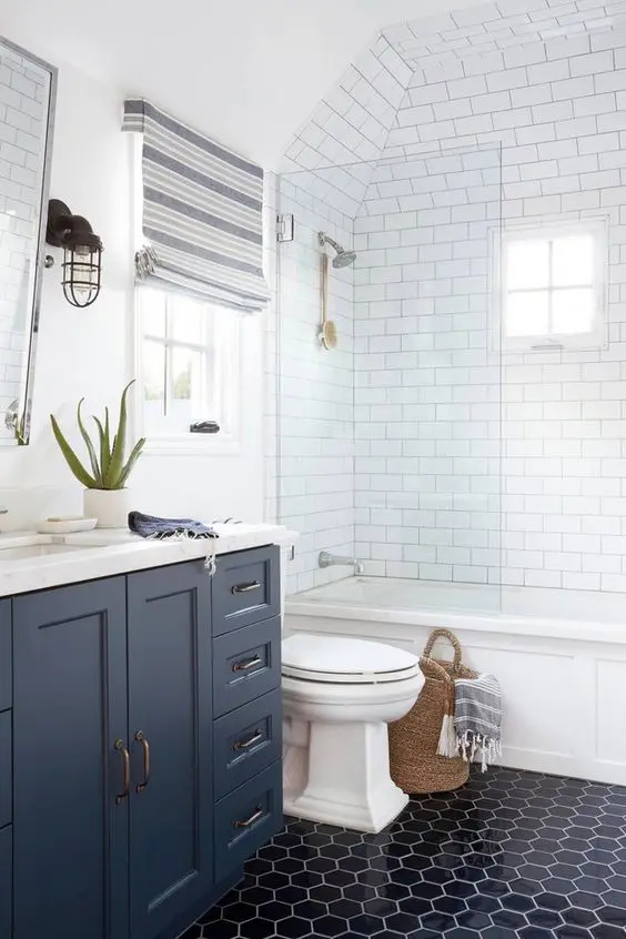 a coastal bathroom with navy hexagon tiles and a navy vanity, striped Roman shades, baksets with striped textiles is cool